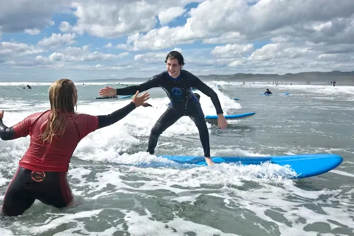 Surfing instructor and student catching gentle waves on beginner boards at Ngarunui Beach.