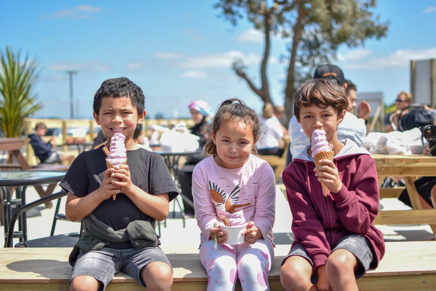 Three children eating ice creams at an outdoor picnic table.